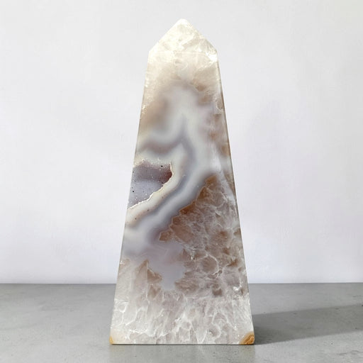 Kindred Crystal Collective — Natural Agate Druzy Obelisk, polished cream-toned crystal tower with flowing grey bands and natural crystalline textures.