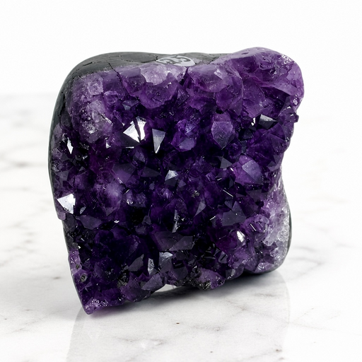 Kindred Crystal Collective — Amethyst Cluster, large deep violet natural Amethyst druzy cluster on dark basalt matrix displayed on white marble surface, angled front view