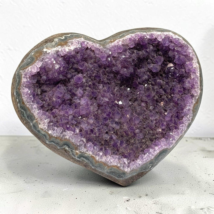 Kindred Crystal Collective — Amethyst Cluster Geode Heart, heart-shaped stone filled with sparkling purple crystal clusters and framed by a polished banded rim.