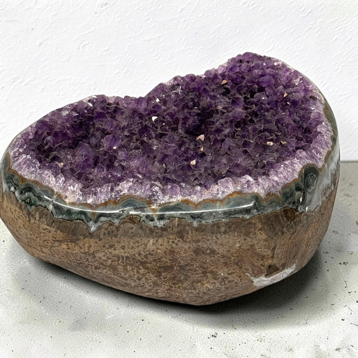 Kindred Crystal Collective — Amethyst Cluster Geode Heart, heart-shaped stone filled with sparkling purple crystal clusters and framed by a polished banded rim.