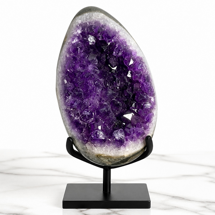 Kindred Crystal Collective — Amethyst Druzy Egg, large open-face Amethyst druzy egg on black metal stand showing deep indigo-violet crystal points and white agate outer shell, marble surface