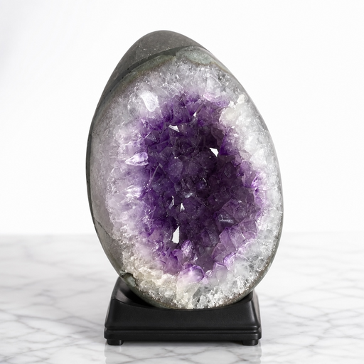Kindred Crystal Collective — Amethyst Druzy Egg, polished dark grey Amethyst druzy egg on black wooden base showing pale lavender and violet crystal cavity, displayed on white marble surface