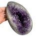Kindred Crystal Collective — Amethyst Geode Egg, hand-held Amethyst geode egg angled to show full egg silhouette with violet crystal cavity, white agate lining and natural basalt rind