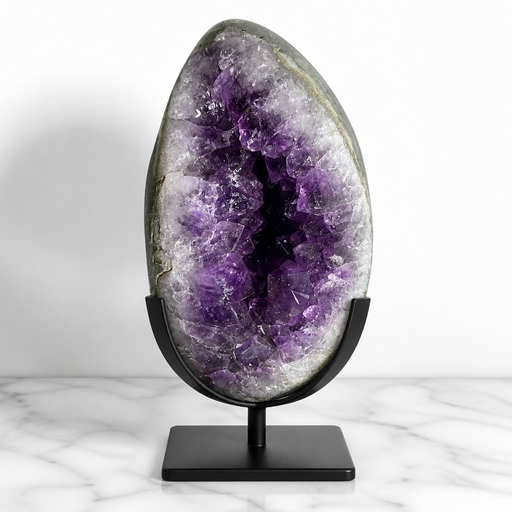 Kindred Crystal Collective — Amethyst Geode Egg, large open Amethyst geode egg on black metal stand showing deep violet crystal cavity and white agate lining, displayed on marble surface