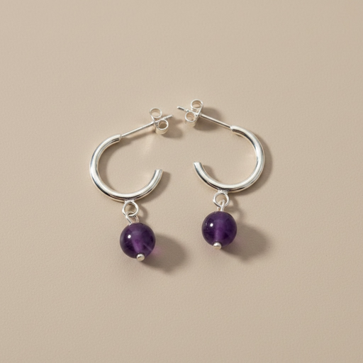 Kindred Crystal Collective - A pair of silver hoop earrings with dangling purple amethyst beads, displayed on a solid beige background.