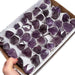 Kindred Crystal Collective — Amethyst Rough Point Boxed, large flat retail box of individually paper-wrapped raw deep purple amethyst points, size reference held in hand