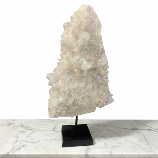 Kindred Crystal Collective - A large Angel Aura Quartz Cluster iridescent white and pale gray translucent points, mounted on a black display stand against a white studio background, with a white marble surface below.