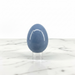A polished blue stone egg displayed upright on a clear acrylic stand against a white marble surface and white background.