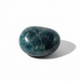 Kindred Crystal Collective — Apatite Free Form, glossy rounded teal-blue stone with dark mottled patterns held in a hand against a white background.