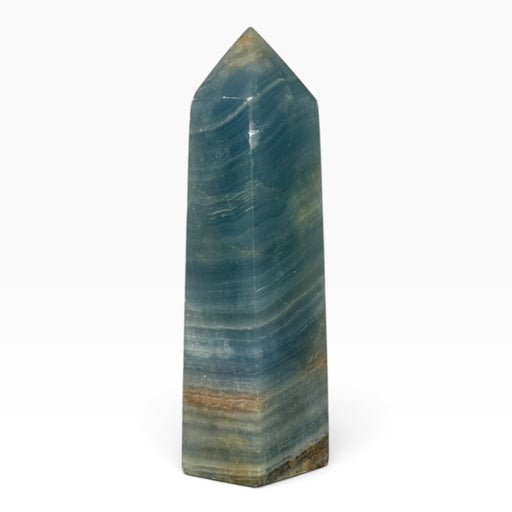 Kindred Crystal Collective — Blue Onyx Obelisk, polished blue-teal stone tower with pale flowing bands, earthy accents and a pointed tip.