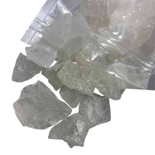  Kindred Crystal Collective — Clear Quartz Rough 1kg, clear-to-cloudy unpolished quartz pieces spilling from a clear bag onto a white background.