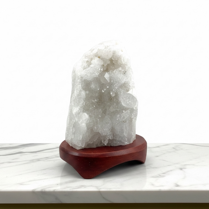 Kindred Crystal Collective - A white crystal geode cluster on a polished reddish-brown wooden display stand, set against a clean white background.