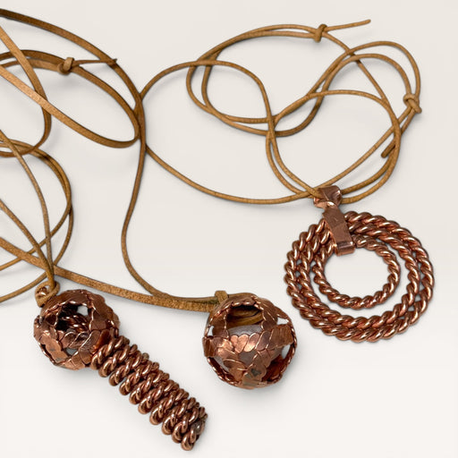 Kindred Crystal Collective - Three copper-toned spiral pendant necklaces with tan cords, displayed on a light off-white background.