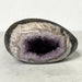 Kindred Crystal Collective — Druzy Amethyst Egg, sparkling purple crystal cavity framed by polished cream, taupe and grey banding, on a light surface.