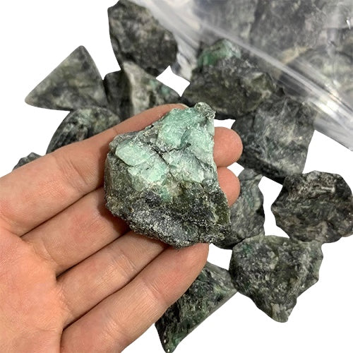 Kindred Crystal Collective — Emerald Rough 1KG, rich green raw emerald chunks spilling from a clear bag on white background.