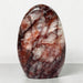 Kindred Crystal Collective — Hematoid Quartz Freeform, polished upright quartz with burgundy and rust-red inclusions through cloudy white stone, on a light surface.