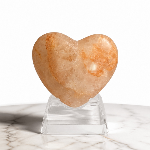Kindred Crystal Collective — Hematoid Quartz Heart, polished warm amber and peach Fire Quartz crystal heart with Hematite inclusions on a clear acrylic stand atop marble surface