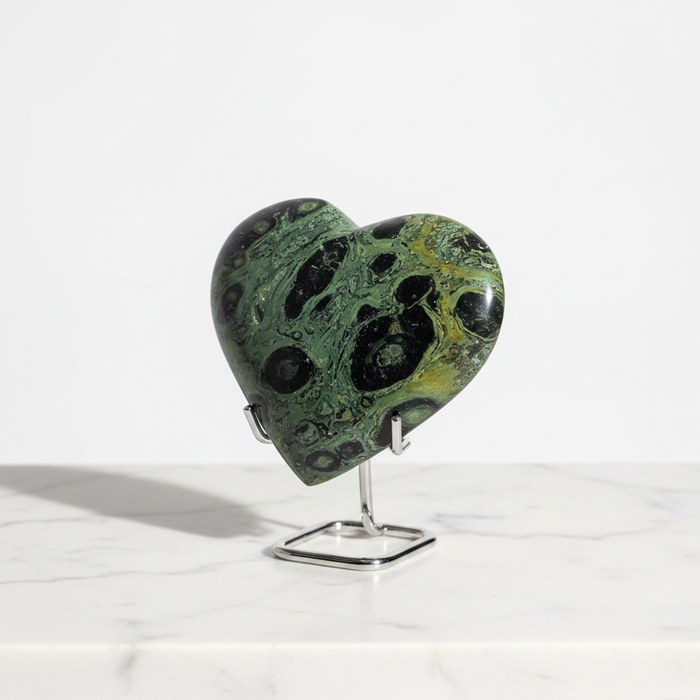 Kindred Crystal Collective — Kambaba Jasper Heart, polished deep green Kambaba Jasper crystal heart with bold black orbicular patterning on clear acrylic stand, white marble surface