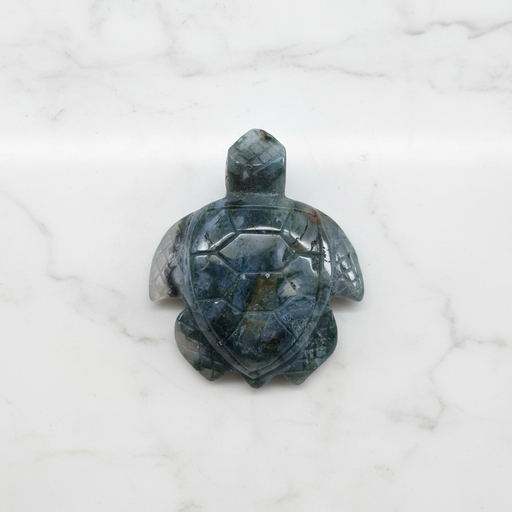 Kindred Crystal Collective - Hand-carved Moss Agate turtle figurine held in a hand, showing deep grey-green stone with detailed shell and flipper carving.