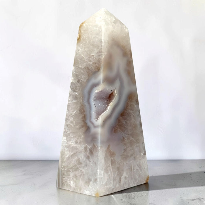 Kindred Crystal Collective — Natural Agate Druzy Obelisk, polished cream-toned crystal tower with flowing grey bands and natural crystalline textures.