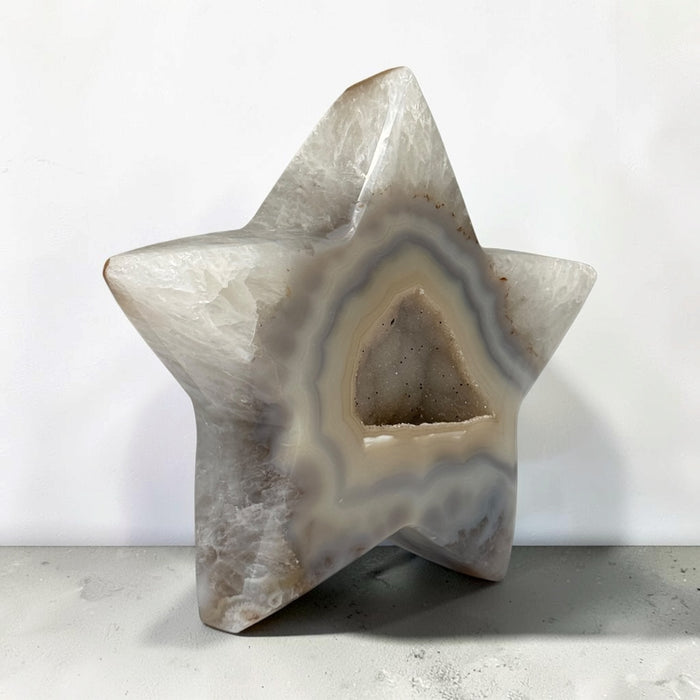 Kindred Crystal Collective — Natural Agate Druzy Star, polished five-point agate star with cream and grey banding surrounding a sparkling druzy cavity, on a light surface.