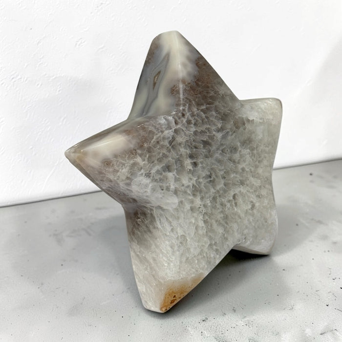 Kindred Crystal Collective — Natural Agate Druzy Star, polished five-point agate star with cream and grey banding surrounding a sparkling druzy cavity, on a light surface.