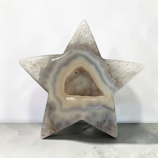 Kindred Crystal Collective — Natural Agate Druzy Star, polished five-point agate star with cream and grey banding surrounding a sparkling druzy cavity, on a light surface.