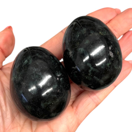 Kindred Crystal Collective - Two polished Nephrite Jade eggs held in an open hand, showing deep dark green colouring with a smooth high-gloss finish.