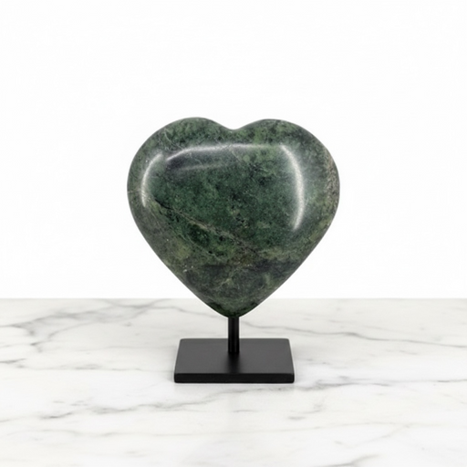 A polished green heart-shaped stone sculpture displayed on a black metal stand, set against a white background with a white marble surface.