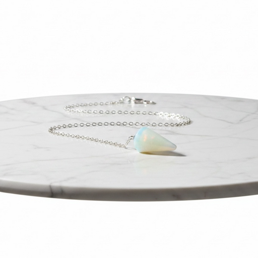 Kindred Crystal Collective — Opalite Pendulum, faceted iridescent opalite pendulum on silver chain, flat lay on marble surface