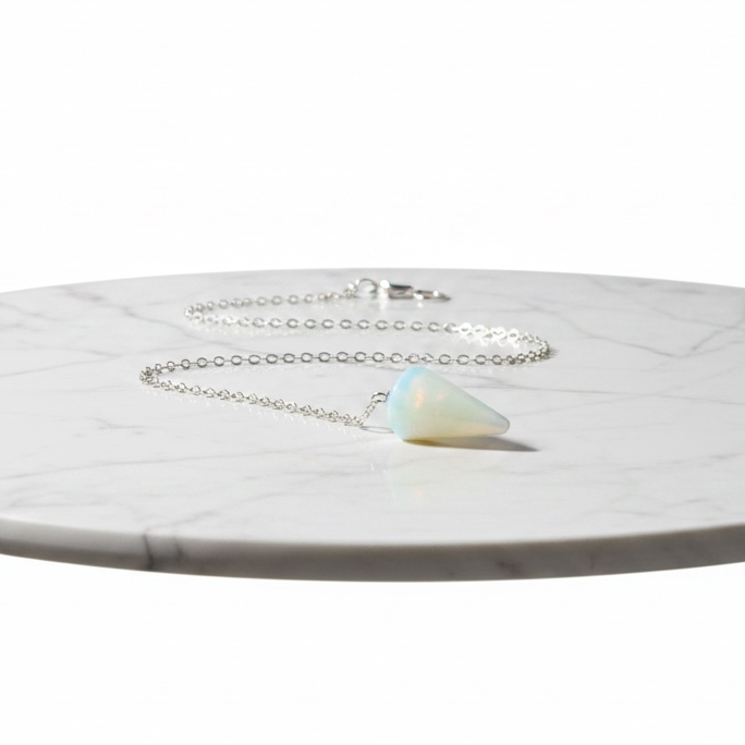 Kindred Crystal Collective — Opalite Pendulum, faceted iridescent opalite pendulum on silver chain, flat lay on marble surface