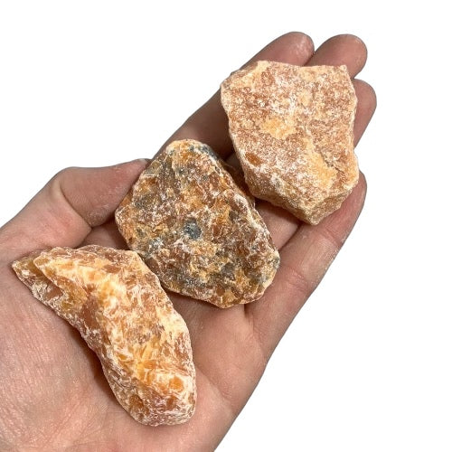 Kindred Crystal Collective — Orchid Calcite Rough 1KG, soft peach and lavender raw calcite chunks spilling from a clear bag on white background.