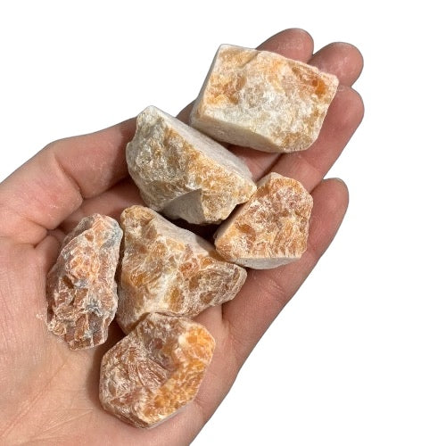 Kindred Crystal Collective — Orchid Calcite Rough 1KG, soft peach and lavender raw calcite chunks spilling from a clear bag on white background.