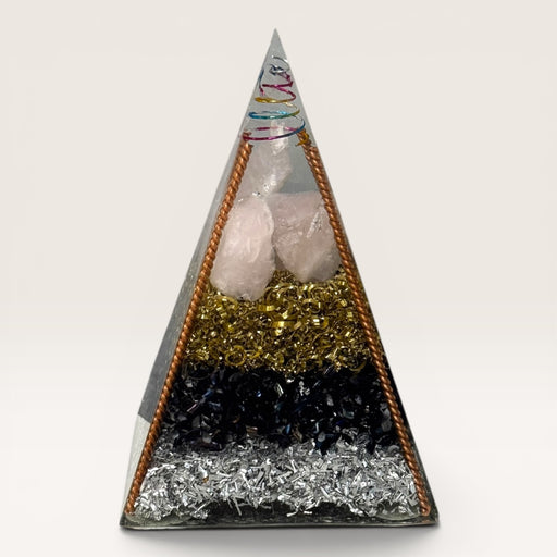 Kindred Crystal Collective — Orgonite Pyramid, handcrafted clear resin pyramid with layered clear quartz, black obsidian, brass shavings, copper frame and multicoloured spiral apex, white background