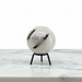 A Quartz Tourmaline Sphere with black inclusions, displayed on a small black metal stand on a white marble surface against a white background.