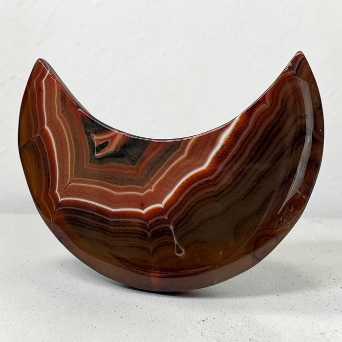 Kindred Crystal Collective — Sardonyx Crescent Moon, polished red-brown and charcoal stone carving with fine white banding.