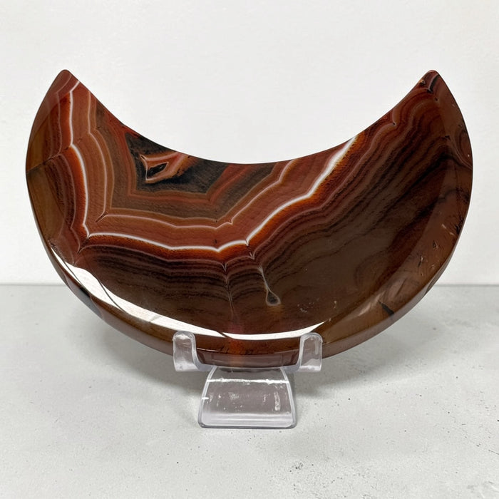 Kindred Crystal Collective — Sardonyx Crescent Moon, polished red-brown and charcoal stone carving with fine white banding.