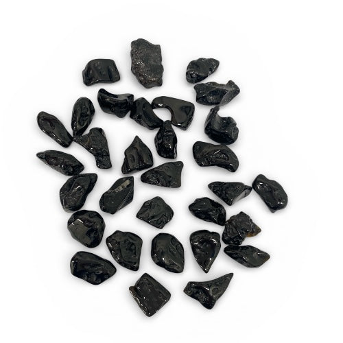 Kindred Crystal Collective — Tektite Natural Specimens, pile of jet black meteorite impact glass fragments showing irregular angular forms, sharp edges and high-gloss glass surface, white background