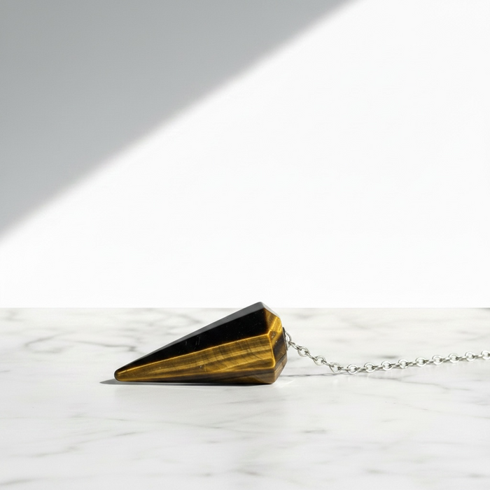 Tigers Eye Gold Pendulum crystal on white background — golden brown chatoyant stone