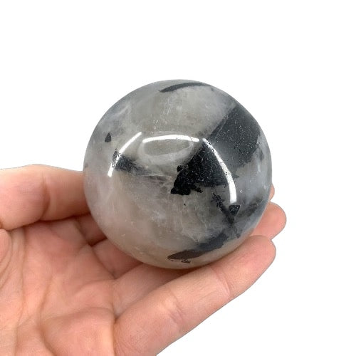 A spherical tourmaline quartz crystal held in a person's hand, with a blurred background.