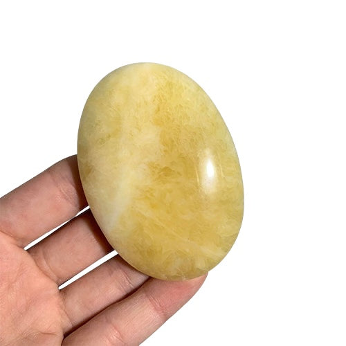 Kindred Crystal Collective — Yellow Calcite Palm Stone, polished oval yellow crystal with pale cream markings held in a hand.