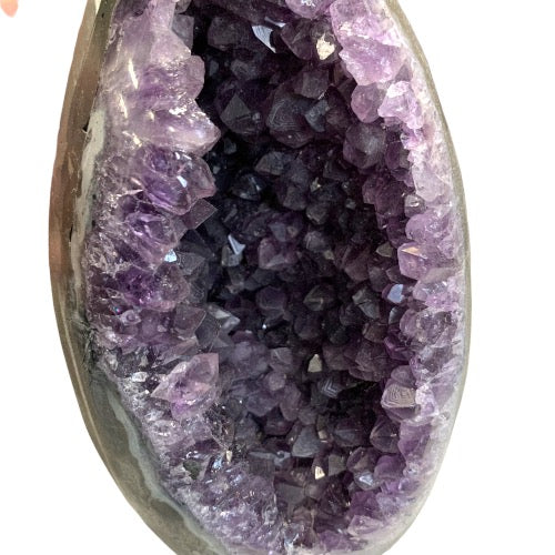Amethyst geode egg close-up showing sparkling purple crystal interior within smooth polished egg shell, a breathtaking statement collector's crystal piece