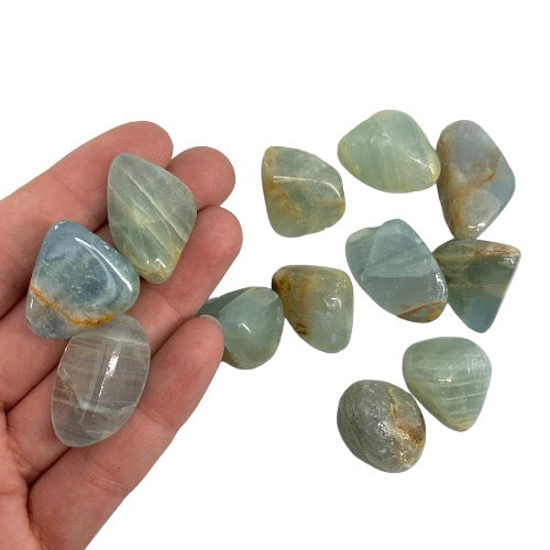 Kindred Crystal Collective — Blue Onyx Tumbled 2–3cm, hand holding three polished seafoam green-blue chalcedony stones with waxy translucent finish and subtle banding