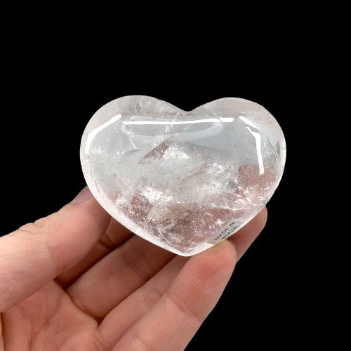 Kindred Crystal Collective — Clear Quartz Heart Brazil, large polished transparent clear quartz heart with natural inclusions, held against black background