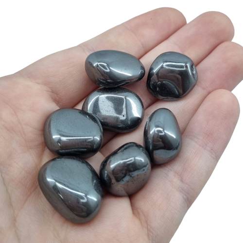 Kindred Crystal Collective — Hematite Tumbled 1.5–2cm, seven polished metallic grey hematite tumbled stones with high-gloss mirror finish held in open palm
