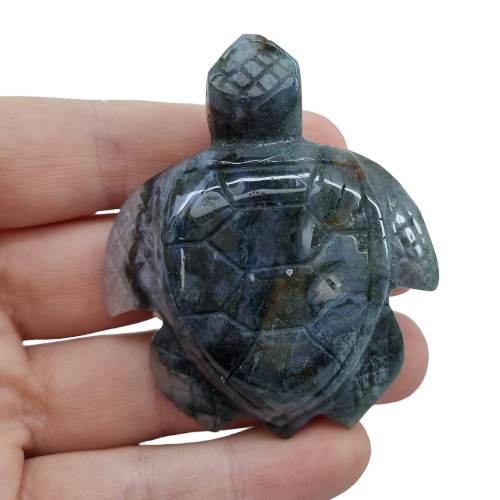 Kindred Crystal Collective - Hand-carved Moss Agate turtle figurine held in a hand, showing deep grey-green stone with detailed shell and flipper carving.