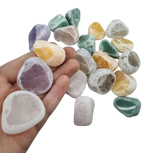Kindred Crystal Collective — Ema Eggs Mixed 500g, eighteen naturally tumbled river stones held in hand showing a mix of amethyst, rose quartz, clear quartz, green and yellow varieties with frosted exterior and polished window